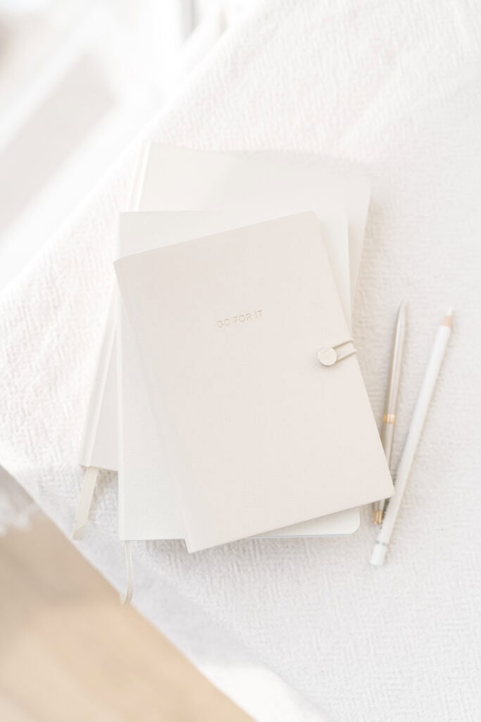 Stack of minimalistic white planners with the phrase "Go For It" on the cover, accompanied by pens, used on a website homepage to navigate to the planners section