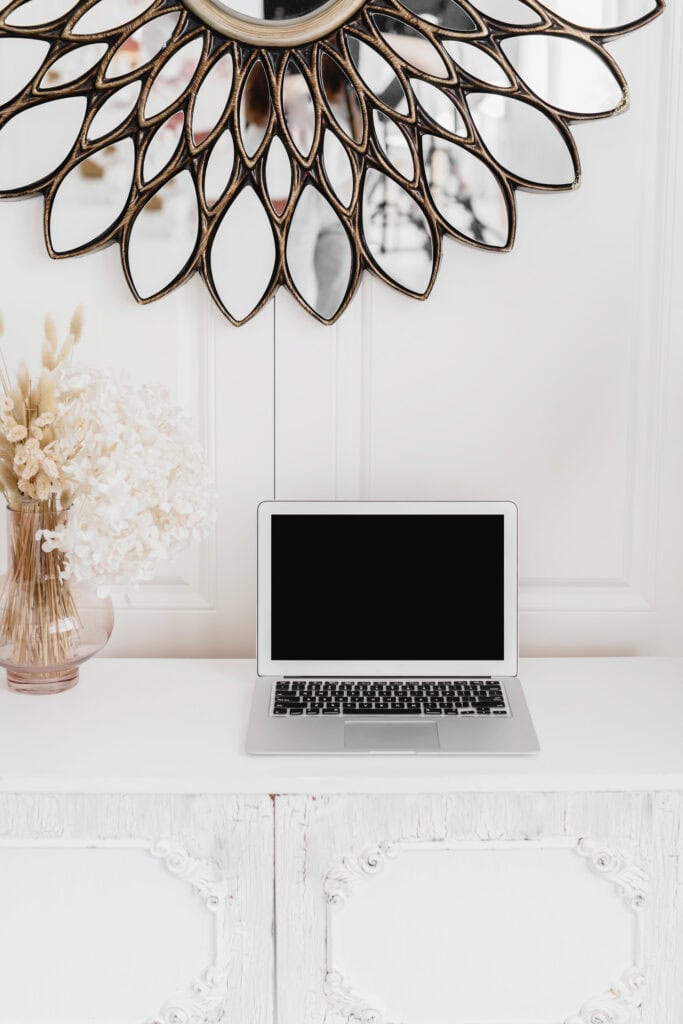  Laptop on a white, ornate table beneath a decorative mirror, with a vase of dried flowers, used on a website homepage to navigate to the blog section with the prompt "I want to read the blog.