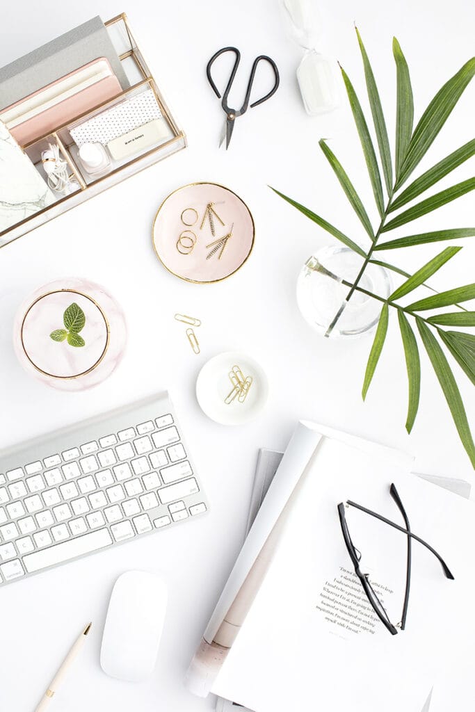 Overhead view of a neatly arranged workspace with a keyboard, scissors, glasses, and decorative items, used on the Print and Hustle homepage to navigate to the home management category of printables.