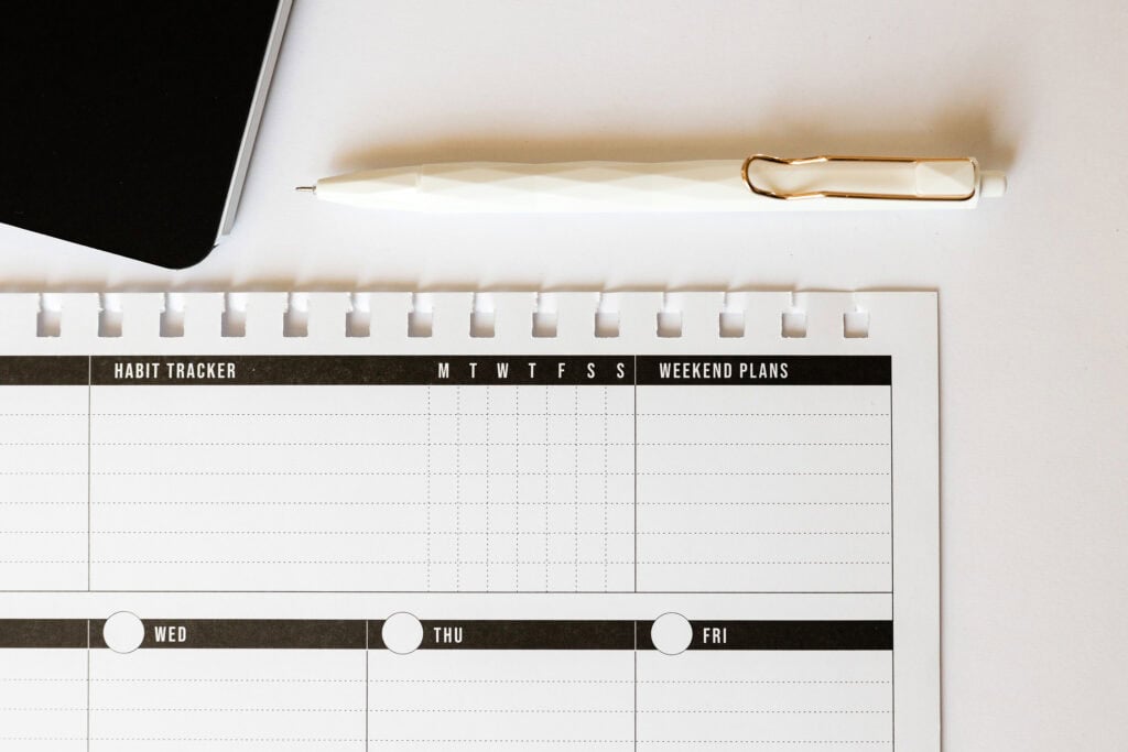 Close-up of a weekly planner with a habit tracker and space for weekend plans, accompanied by a white pen, illustrating essential printables for busy moms.