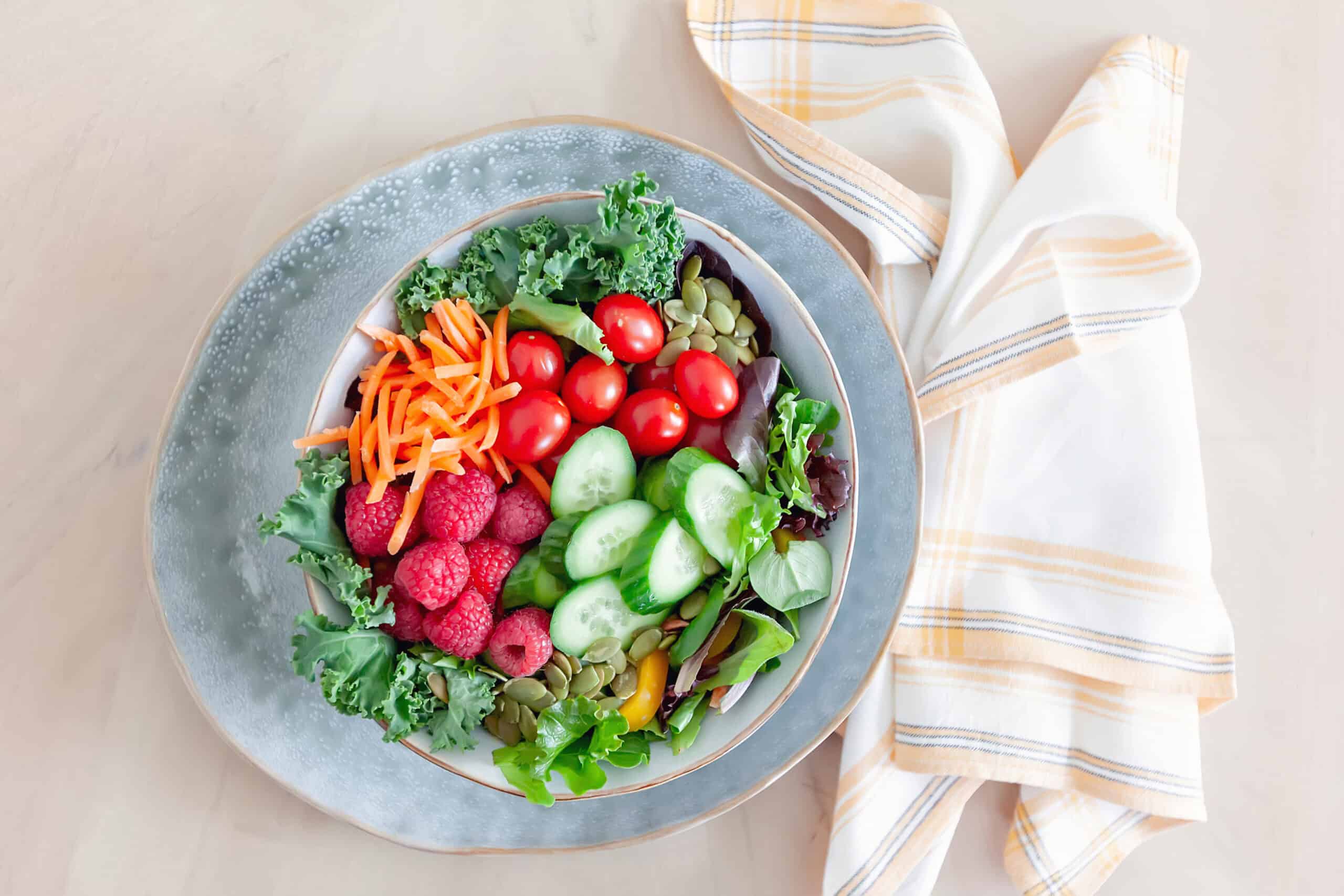 Healthy salad for simple meal planning for busy moms, featuring fresh kale, cucumbers, cherry tomatoes, raspberries, shredded carrots, and pumpkin seeds, perfect for quick and nutritious meals.