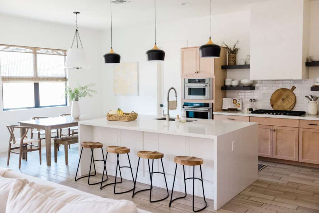  A bright and organized kitchen with a large island, wooden stools, and a cozy dining area, representing a well-managed family space where moms can plan and organize daily tasks.