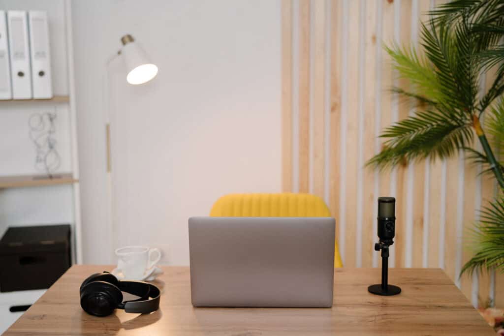 A home office setup with a laptop, microphone, headphones, and a yellow chair, illustrating a workspace for content creation. This image is featured in a post on printandhustle.com about the best flexible side hustles for stay-at-home moms.
