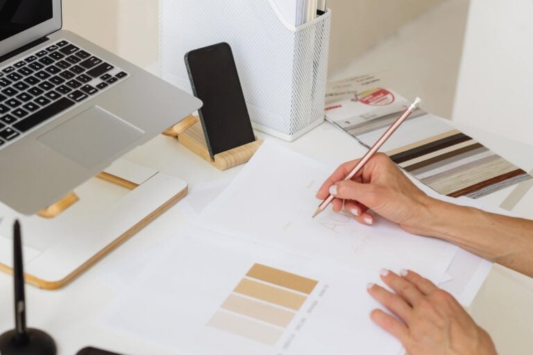 Hybrid planner system setup with a laptop on a stand, smartphone, and a person writing on printable planner pages with a pencil. Shows how digital and printable planners can be used together for an organized workflow.