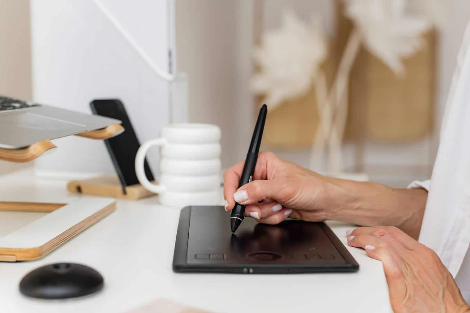 Entrepreneur using a digital tablet and stylus at a desk with a laptop, smartphone, and coffee mug. Represents hybrid planning for entrepreneurs who use digital tools like Notion, Trello, and ClickUp to manage projects and tasks.