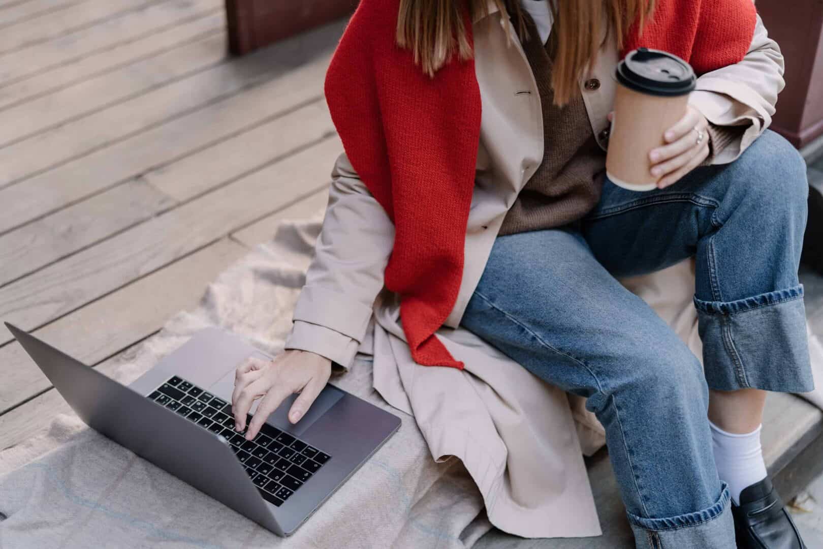 Mom sitting outdoors with a laptop on her lap and a coffee cup in hand. Represents hybrid planning for moms, showing how digital tools and flexible planning systems help balance family schedules and personal tasks.