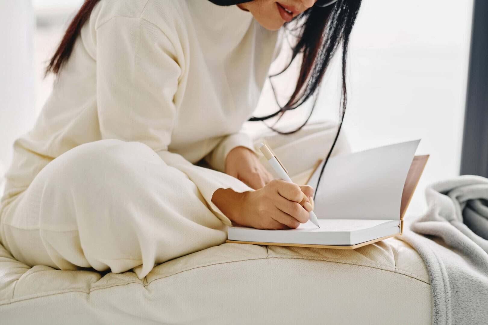 Woman relaxing on a sofa with a notebook and coffee, wrapped in a cozy blanket. Represents a monthly planner review routine for reflecting on goals and planning ahead.
