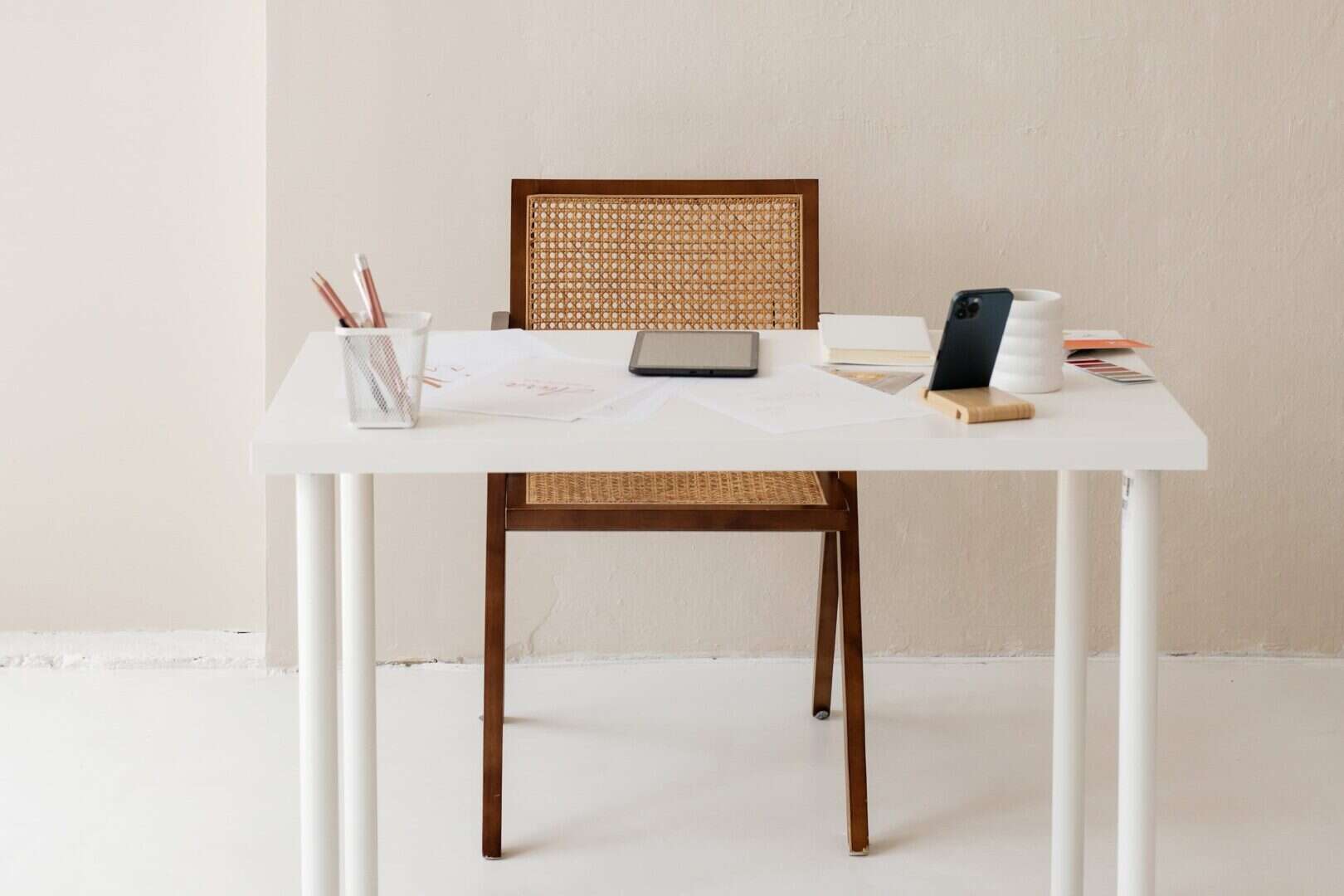 Minimal home office desk with scattered papers, tablet, smartphone on a wooden stand, coffee mug, and pencil holder. Captures a realistic planner desk setup that shows how moms and entrepreneurs juggle planning, organization, and daily tasks before diving into FAQs.