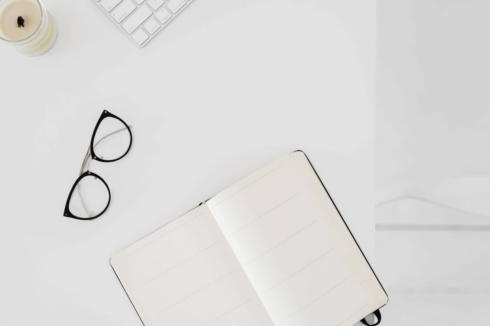 Open lined planner on a white desk with black eyeglasses, keyboard, and candle. Represents a planner reset routine for building consistent daily, weekly, and monthly planning habits.