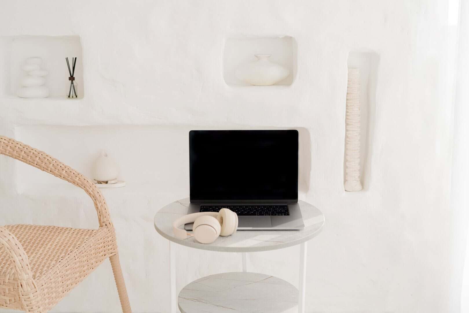 Minimal workspace with a laptop and headphones on a round table beside a woven chair. Represents creating a planner routine that sticks by setting up a consistent, distraction-free space for daily and weekly planning habits.