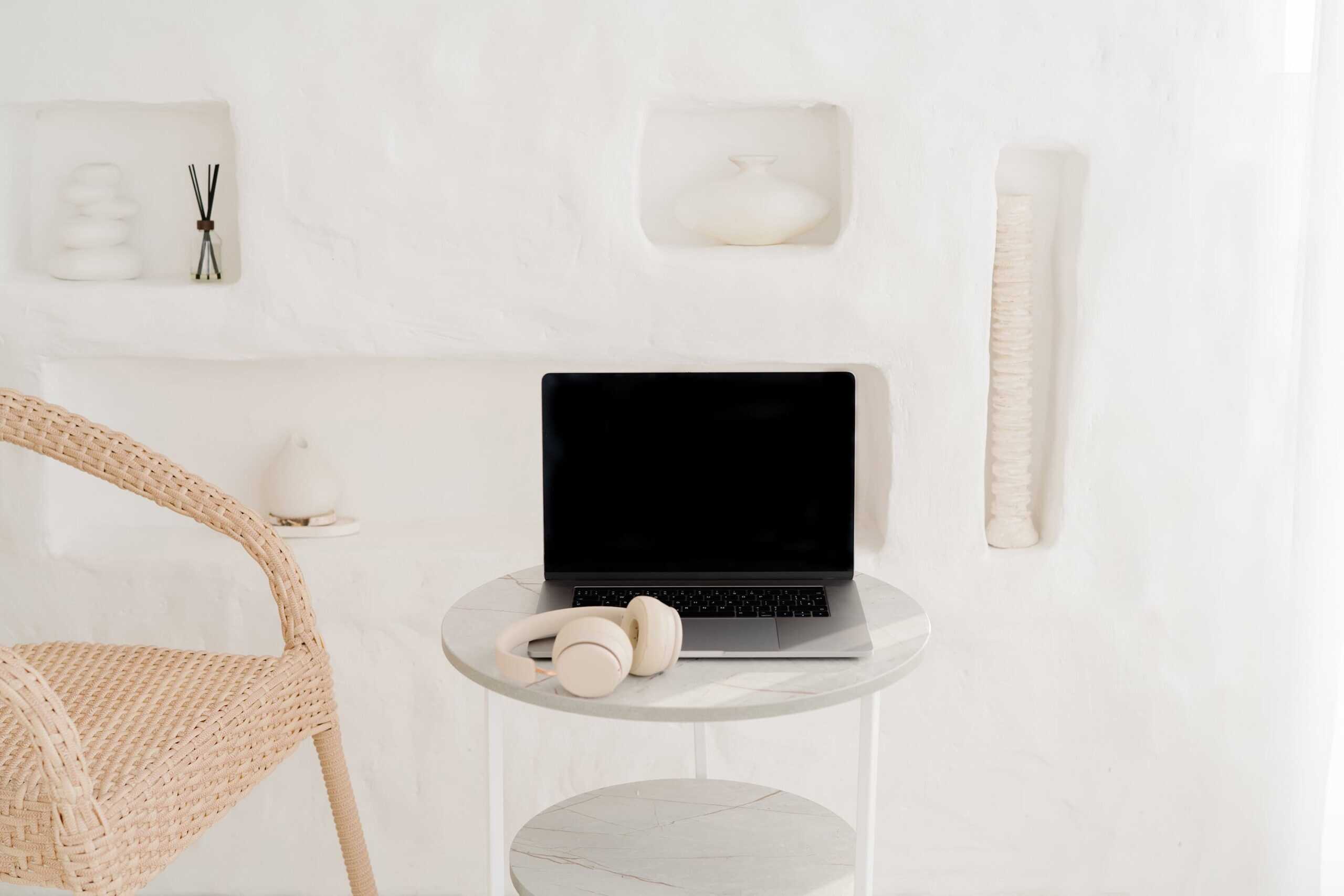 Minimal workspace with a laptop and headphones on a round table beside a woven chair. Represents creating a planner routine that sticks by setting up a consistent, distraction-free space for daily and weekly planning habits.