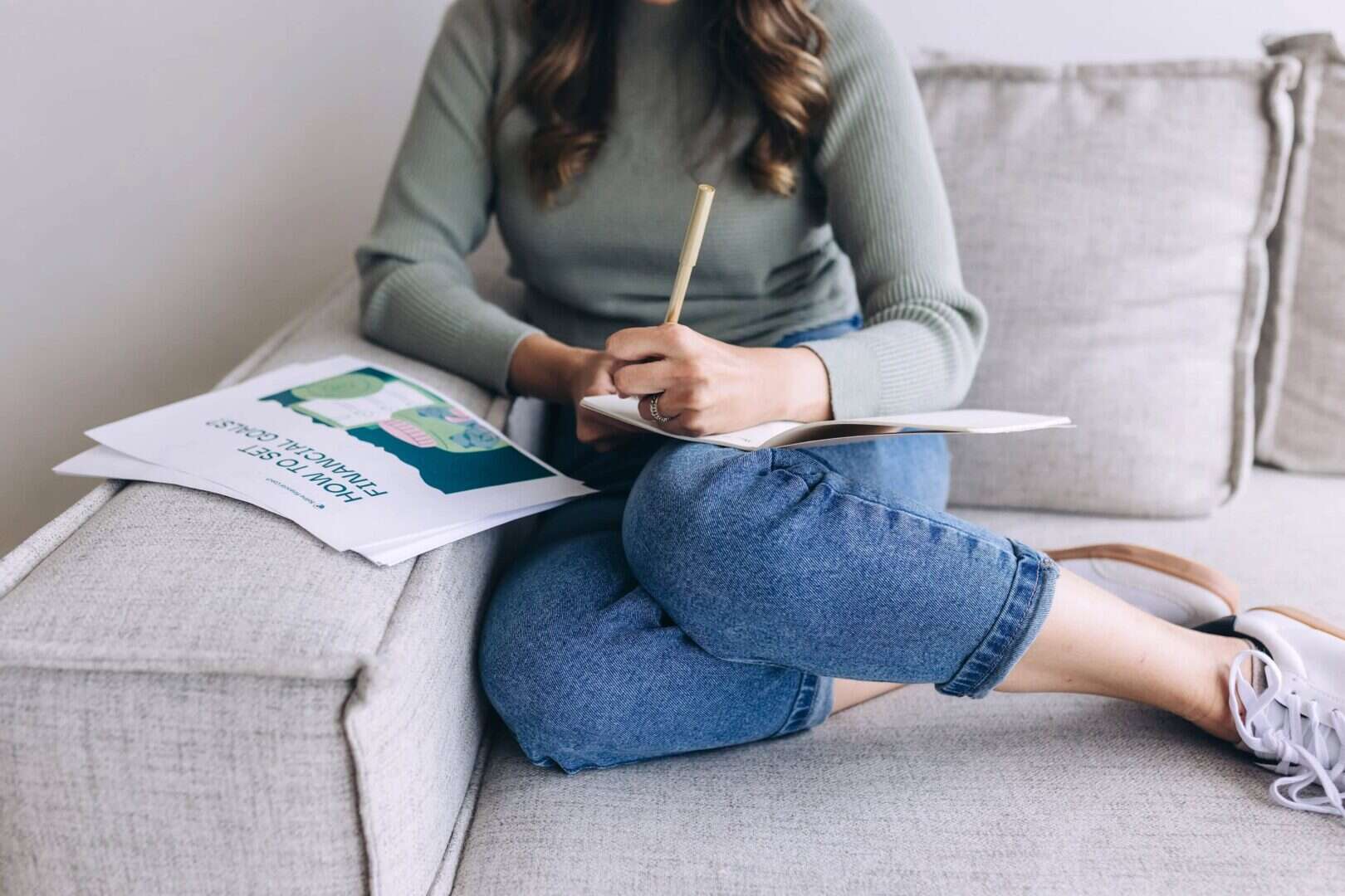 Mom sitting on couch writing in notebook, showing relaxed lifestyle with printable planners for moms.