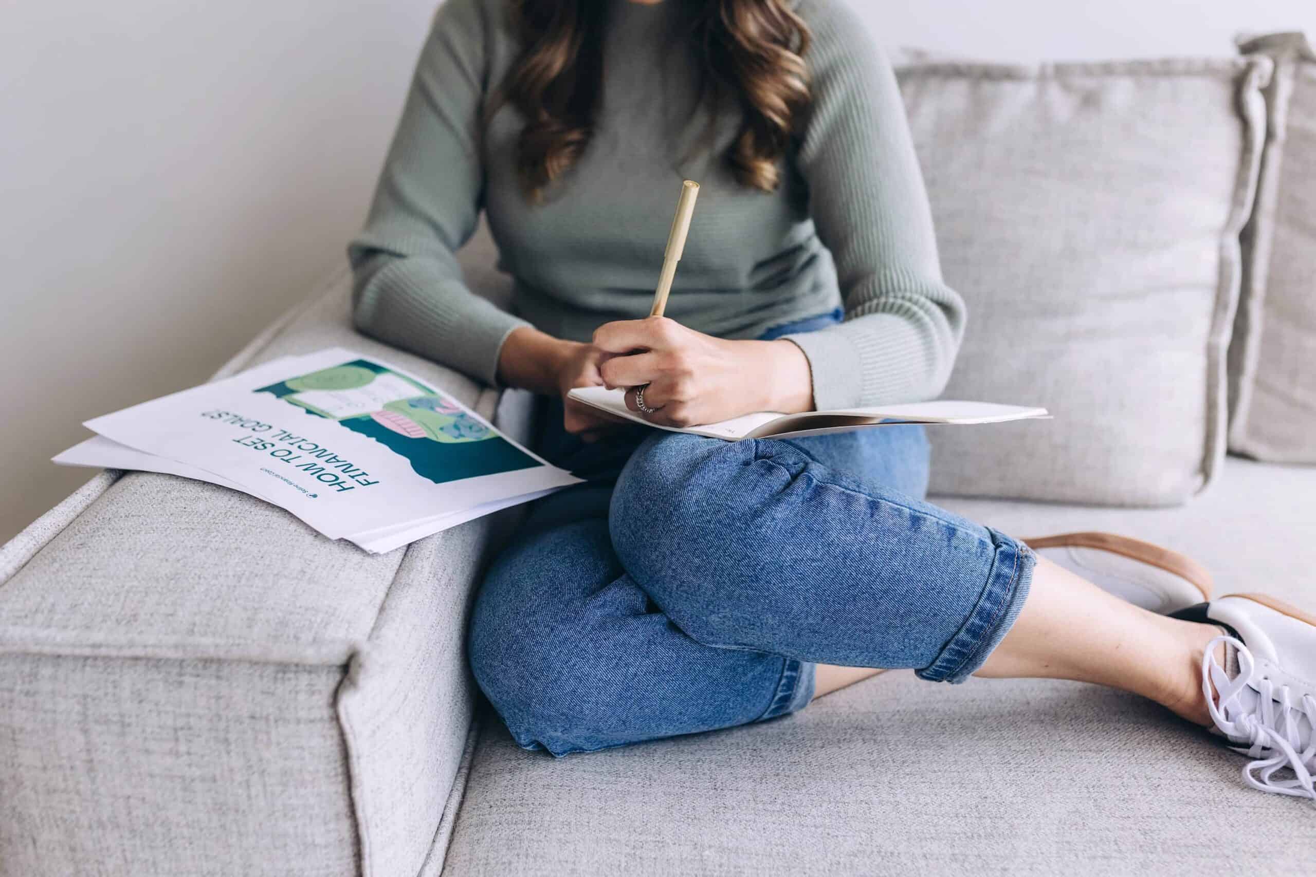 Mom sitting on couch writing in notebook, showing relaxed lifestyle with printable planners for moms.