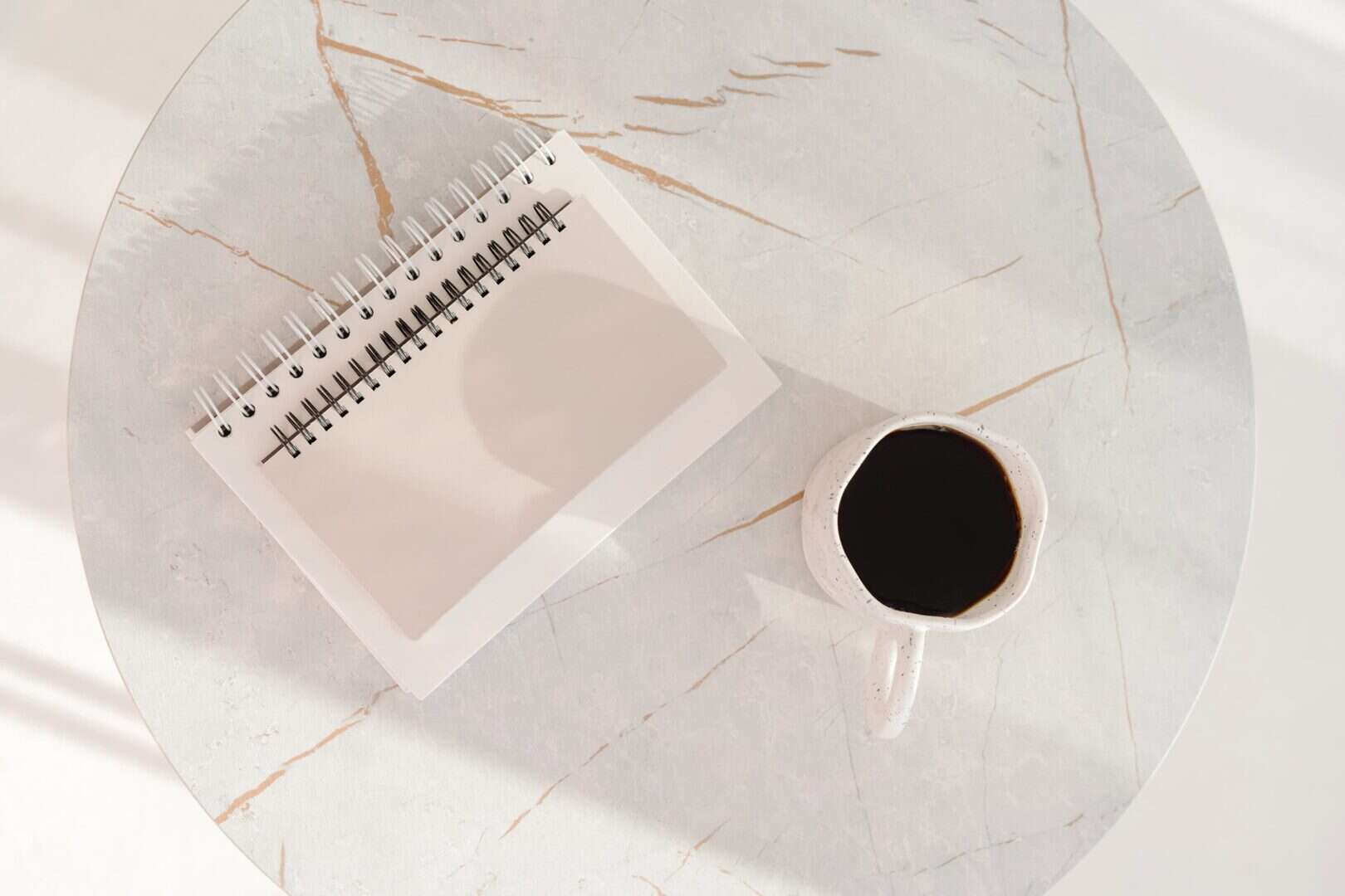 Spiral notebook on a marble table beside a cup of black coffee. Represents a weekly planner routine or reset session, creating space to reflect, plan ahead, and build consistent habits.