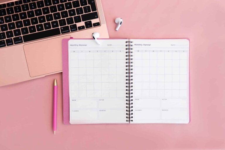 Open monthly planner beside pink laptop and pen, showing digital vs printable planners setup for organized planning.