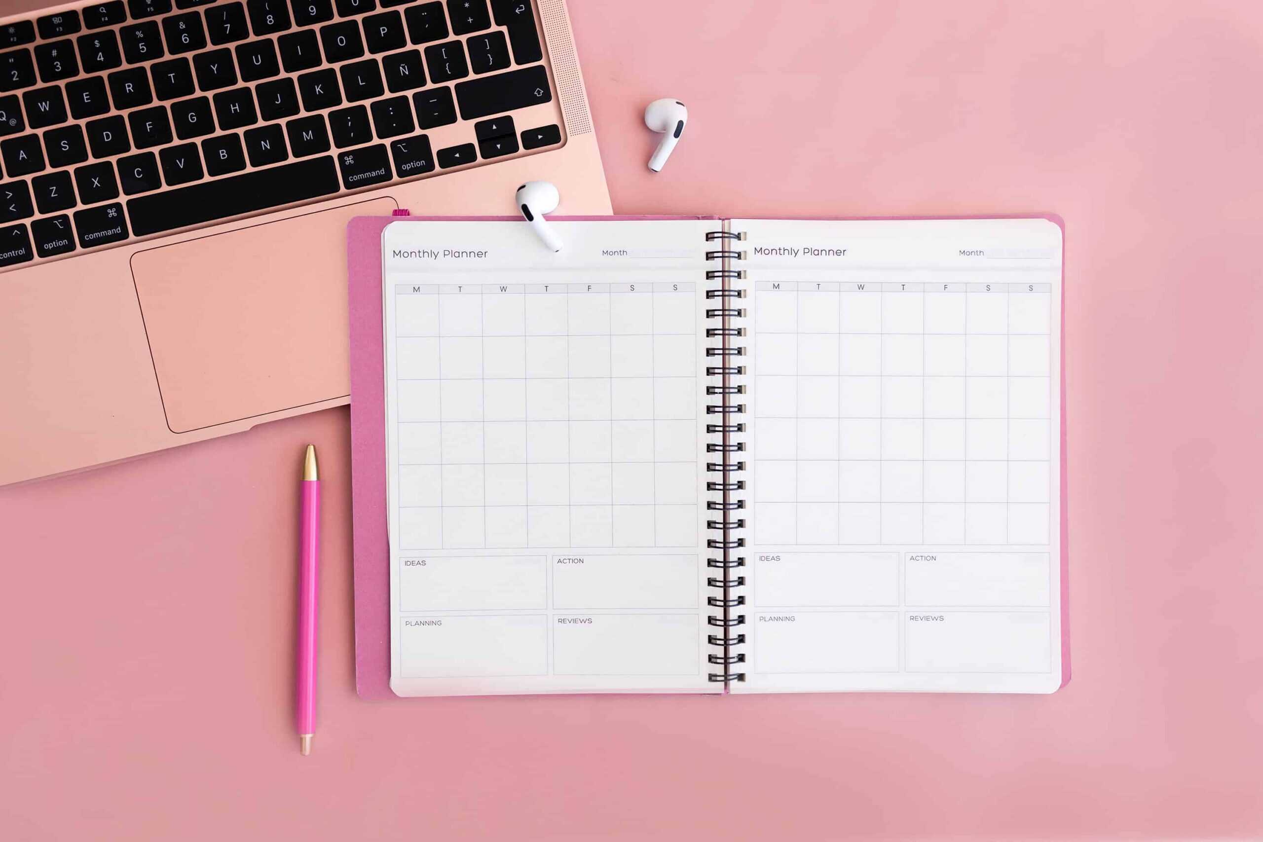 Open monthly planner beside pink laptop and pen, showing digital vs printable planners setup for organized planning.